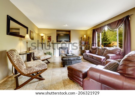 Luxury living room interior with fireplace. Furnished with burgundy leather couches, black ottoman and zebra print chairs