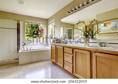 Spacious bathroom interior with window. View of bathroom vanity cabinet, white bath tub and glass door shower