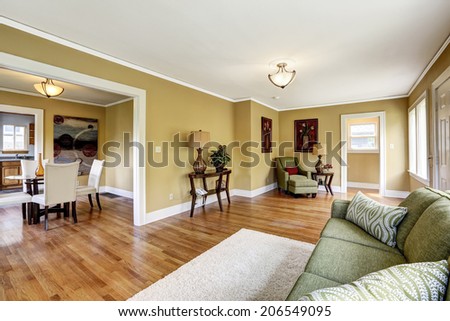 House interior with open floor plan. Room furnished with green sofa and armchair. View of dining table set in kitchen room