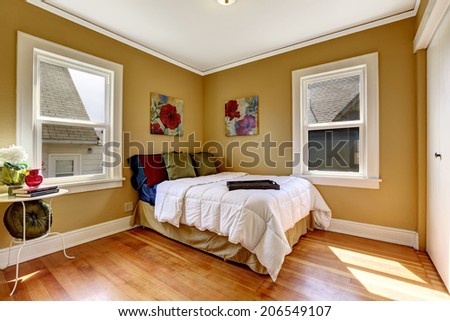 Small bright room with  windows and hardwood floor. View of single bed with colorful bedding and old table