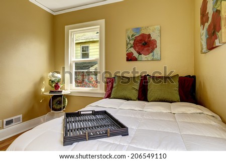 Small bright room with  windows and hardwood floor. View of bed with green and burgundy pillows