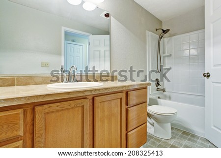 Light tones empty bathroom with tile floor, white bath tub and wooden vanity cabinet