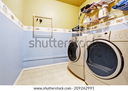 Laundry room interior in light blue and yellow colors. View of washer and dryer