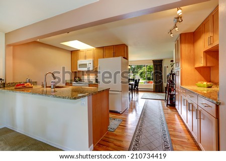 Kitchen room with white appliances and light tone cabinets. View of walk-through hallway with rug
