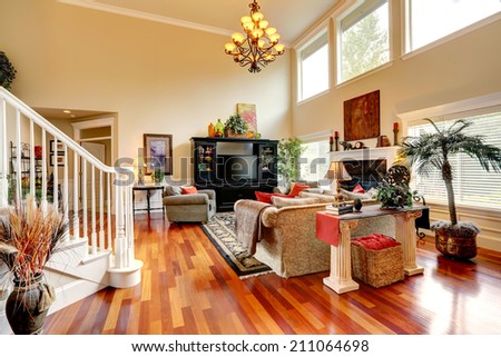 Living room interior with high ceiling. Furnished with comfortable sofa, black cabinet with tv, decorated with fake trees