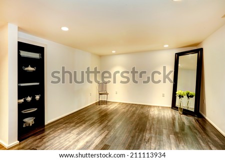 Empty dining room with hardwood floor and soft ivory walls. Room decorated with large mirror and open storage cabinet with dishes