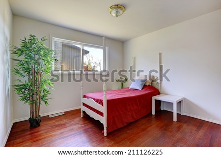 White bedroom with hardwood floor. View of bed with high poles. Room decorated with fake bamboo tree