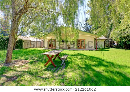 House backyard with green lawn and wooden table with benches