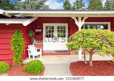 Beautiful red American classic farm house with green lawn. View of entrance porch with walkway and garage with driveway