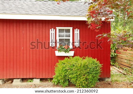 Beautiful red American classic farm house with green lawn. View of entrance porch with walkway and garage with driveway
