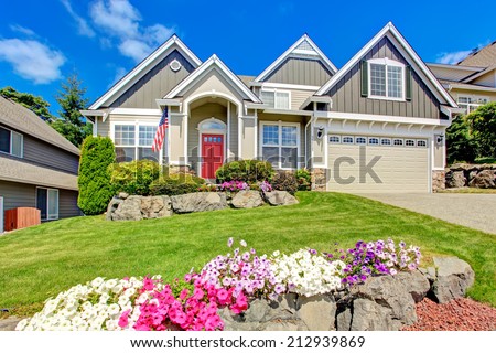 Grey house exterior with entrance porch and red door. Beautiful front yard landscape with vivid flower and stones