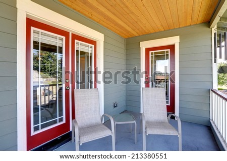 Entrance porch with chairs and small table. Glass entrance doors with red trim
