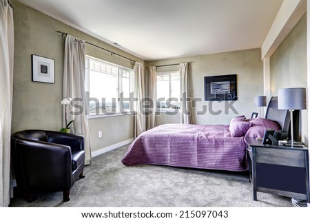 Simple bedroom interior in light grey tones with bright purple bed and leather chair