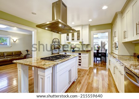 Modern and practical kitchen room design. White cabinet with granite tops, kitchen island with built-in stove and steel hood