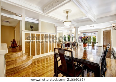 Luxury spacious dining room with hardwood floor, wood wall trim and coffered ceiling. Room in brown and white tones