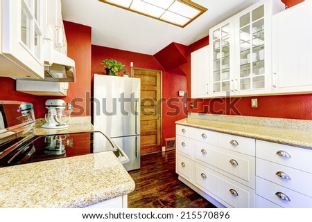 Kitchen room with bright red wall and white cabinets with granite tops