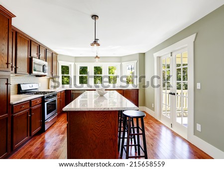 Spacious kitchen room in mint color with french door, bright wooden cabinets and island with stools