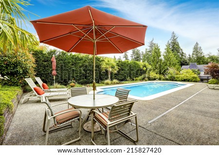 Backyard with swimming pool, deck chairs and patio table with umbrella