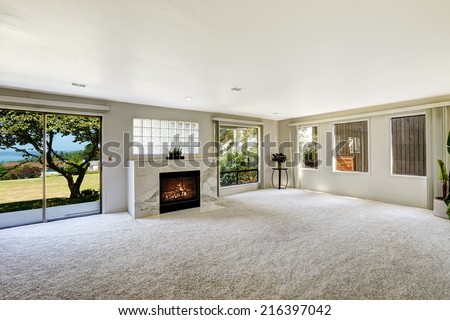 Bright empty room with fireplace and carpet floor. Glass slide door to backyard
