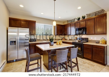 Modern kitchen room with kitchen island and stools. Dark brown cabinets, steel appliances and tile floor
