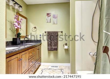 Bright bathroom in light green tone. Wooden cabinet with granite top decorated with flowers.