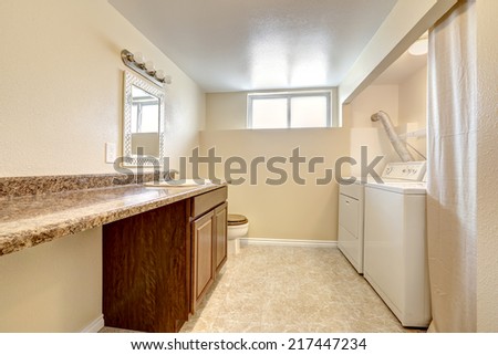 Bright laundry room with ivory walls. Cabinet with granite counter top and mirror