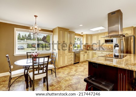 Spacious kitchen room with tile back splash trim and tile floor. Big kitchen island with built-in stove, granite top and steel hood. Dining area