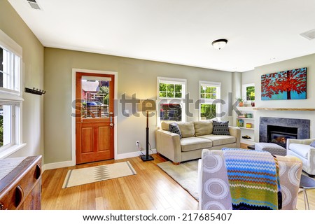 Bright very small room with fireplace, sofa and armchair. View of entrance door with rug on hardwood floor