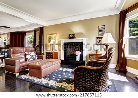 Luxury home interior in brown tones with fireplace, antique chairs, leather couch and ottoman