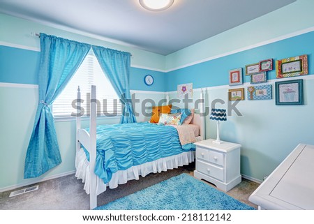 Happy girls room interior in light blue tones. White bed with high poles and blue bedding, blue rug and curtains