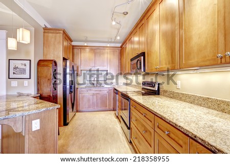 Spacious kitchen room with wooden storage cabinets, granite tops, steel appliances and island