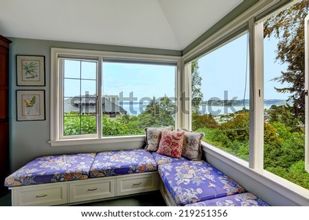 Cozy sitting area in bedroom with bay view. Bench with drawers and purple floral pillows create comfort in bedroom