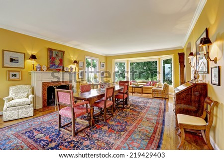 Yellow bright dining room with antique carved wood table, old colorful rug.