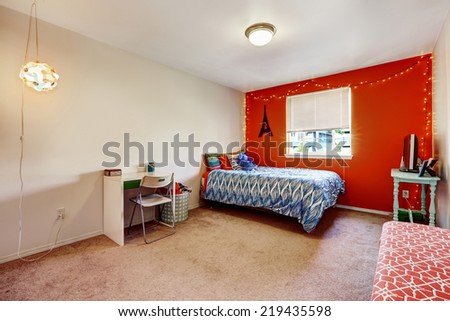 Bedroom interior with bright red wall. Furnished with a single bed, desk and table with tv