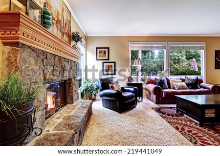 Luxury family room with cozy stone trimmed fireplace. Rich leather couch and armchair create comfort atmosphere