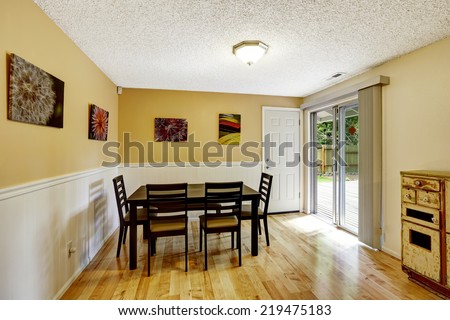Dining room with light yellow walls and white trim. Simple black dinig table set. Room has exit to backyard patio area