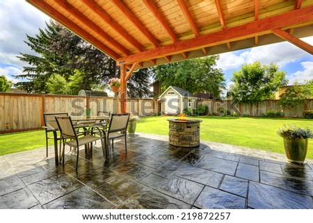 Pergola with patio area. Tile floor decorated with flower pots. Stone trimmed fire pit and  patio table set