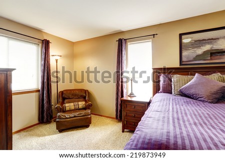 Master bedroom interior. Rich furniture set with bright purple bedding and pillows. Leather armchair in the corner