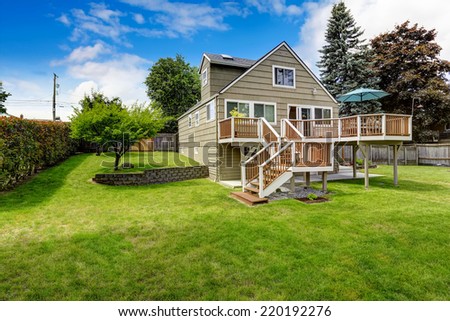 Big house with walkout deck in brown and white trim. Spacious backyard area with trees