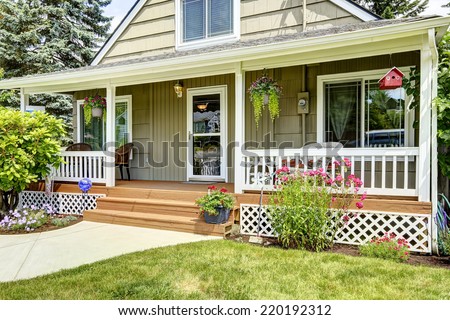 House with cozy entrance porch. White railings blend with brown wooden floor and green house exterior