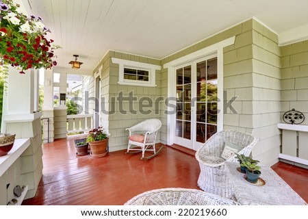 Entrance porch in old house with wicker chairs and glass entrance door. Porch decorated with flower pots