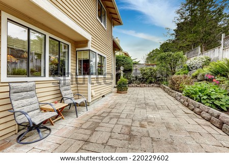 Backyard area with stone tile floor and beautiful flower bed. Sitting area with two chairs and small coffee table