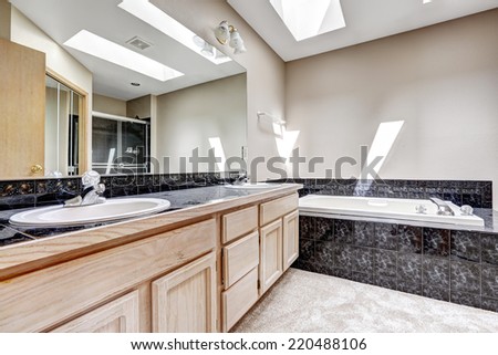 Bright bathroom interior with carpet floor, white bath tub with black granite tile trim. Vanity cabinet with granite top and large mirror