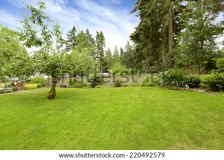 Old wooden fence with trees, bushes and lawn. FLower bed with brick trim
