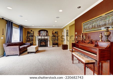 Simple living room with fireplace and couch.  Burgundy wall and piano decorated with vase