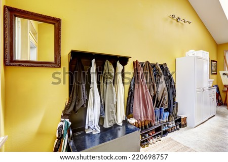 Bright yellow hallway with white wardrobe and black furniture full of hanging clothes and shoes