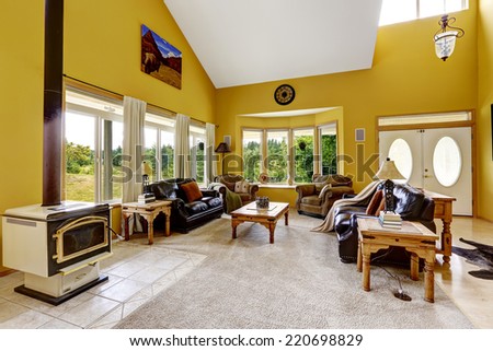 Beautiful luxury house with high vaulted ceiling and bright yellow walls. Spacious family room with leather couches, wooden tables and  antique stove