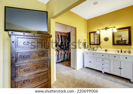 Bright yellow room with white vanity cabinet, wooden dresser with tv and walk-in closet