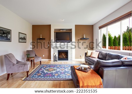 Light brown tone living room with fireplace and tv. Comfort leather couch with pillows and orange blanket