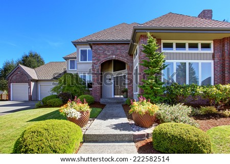 Big luxury house with tile roof and brick wall trim. Green landscape with flower pots